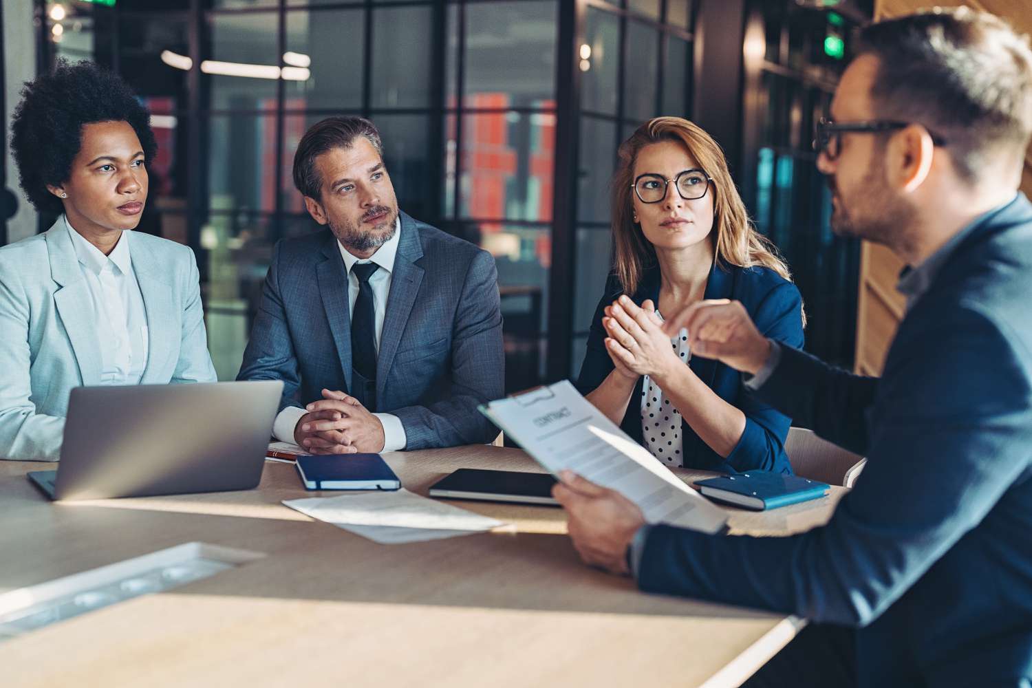 Business professionals in a modern office reviewing crypto banking documents on laptops, representing step-by-step process for opening a crypto business account in 2024.
